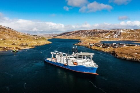 Image of specialist cable laying vessel the NKT Victoria. The ship is waiting in waters off Weisdale Voe, with a rugged landscape behind the ship.